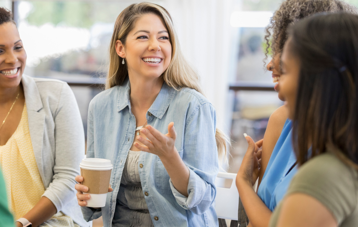 a group of women are sitting around a table talking and drinking coffee .