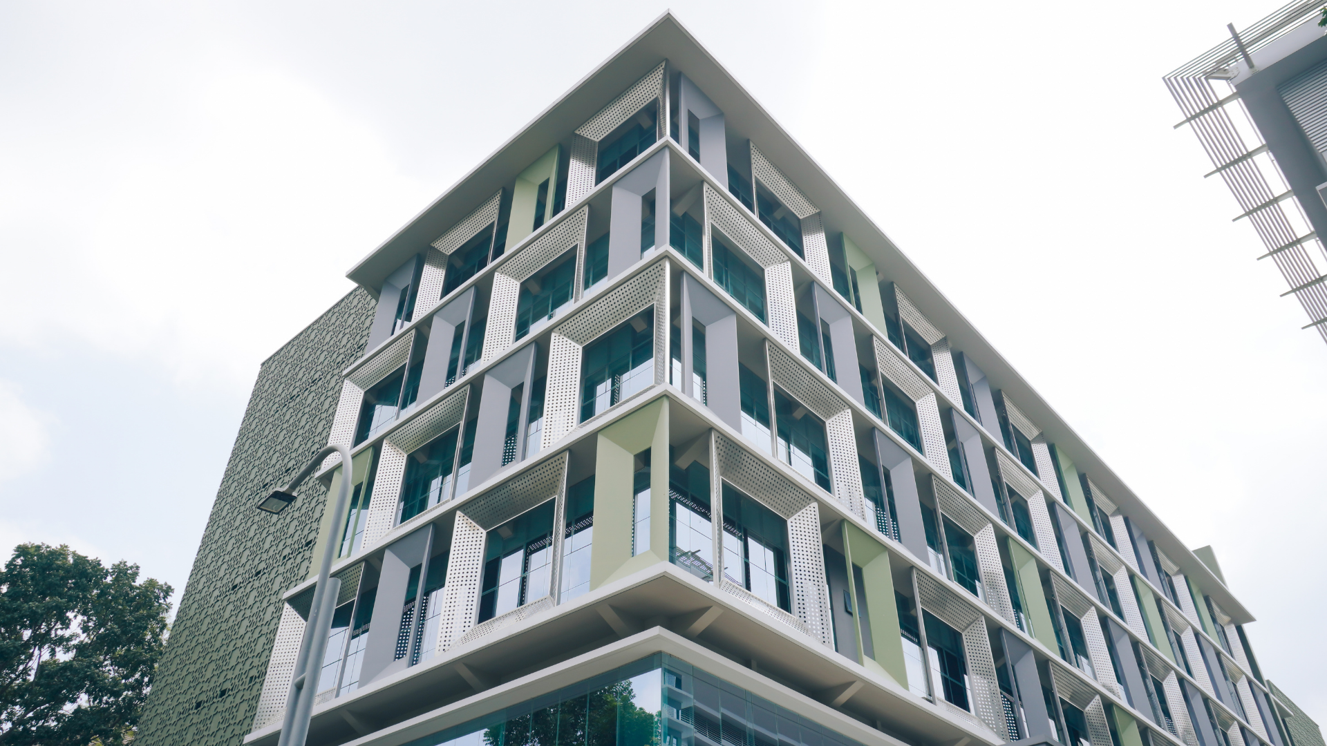 A modern, multi-story building featuring geometric, light-colored facade panels and recessed windows against a cloudy sky.