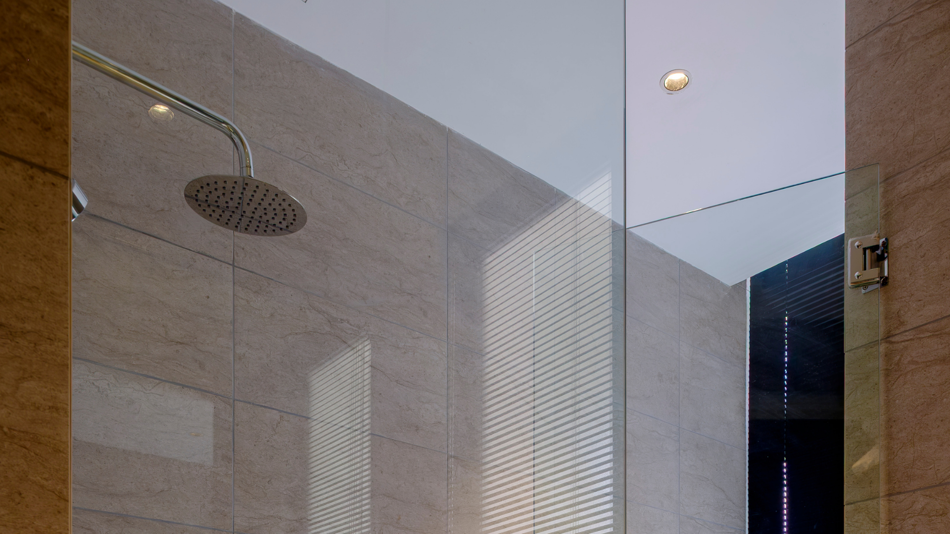 Modern shower with a round overhead showerhead, tiled walls, and a glass partition in a contemporary bathroom.