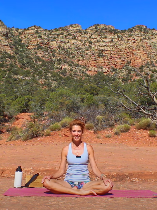 A woman is sitting in a lotus position on a yoga mat in the desert.