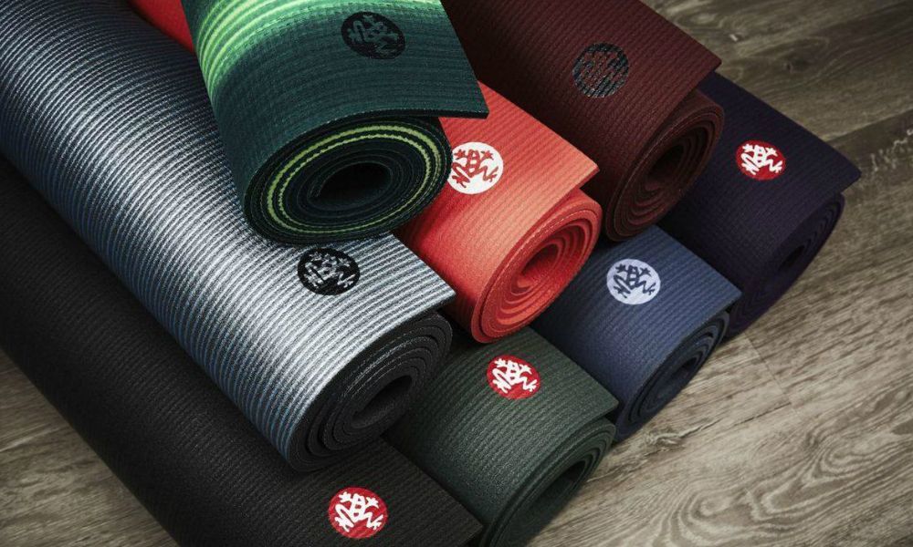 A bunch of yoga mats are stacked on top of each other on a wooden floor.