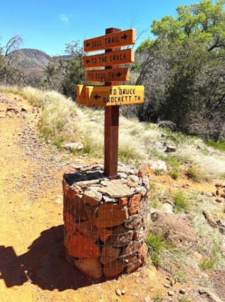 A wooden sign on a stone pillar points to various trails
