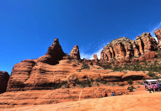 A group of people are standing in front of a large rock formation.