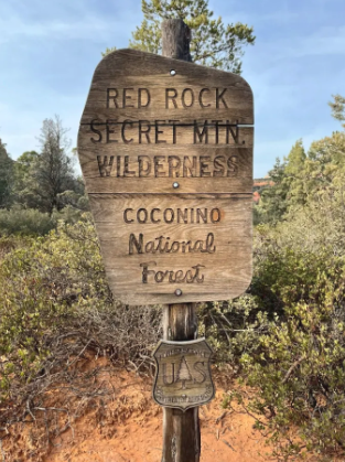 A wooden sign that says red rock secret min wilderness coconino national forest