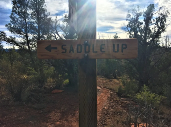 A wooden sign that says saddle up on it
