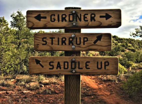 A wooden sign that says girdner stirrup and saddle up