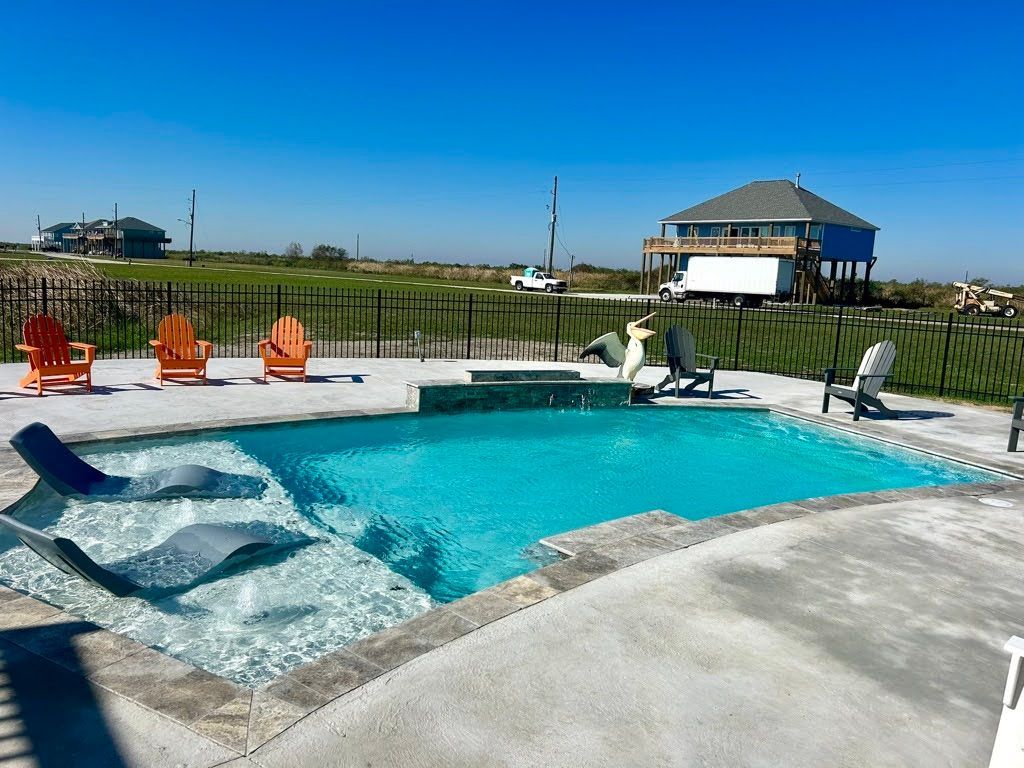 A large swimming pool surrounded by chairs and a fence with a house in the background.