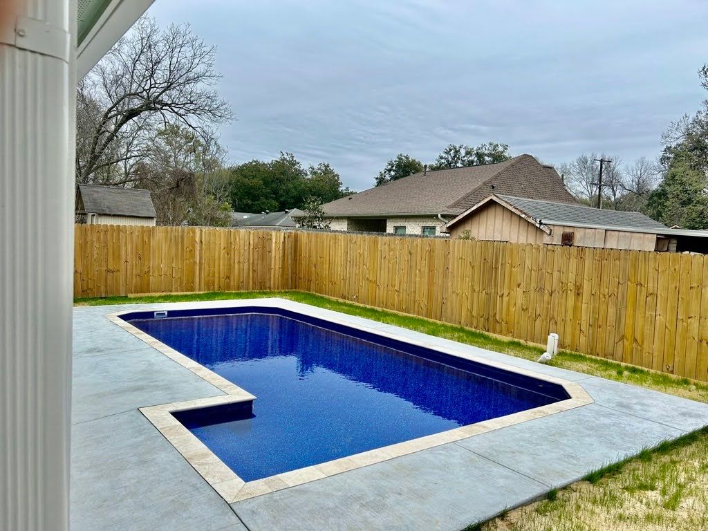 A large swimming pool in the backyard of a house with a wooden fence.