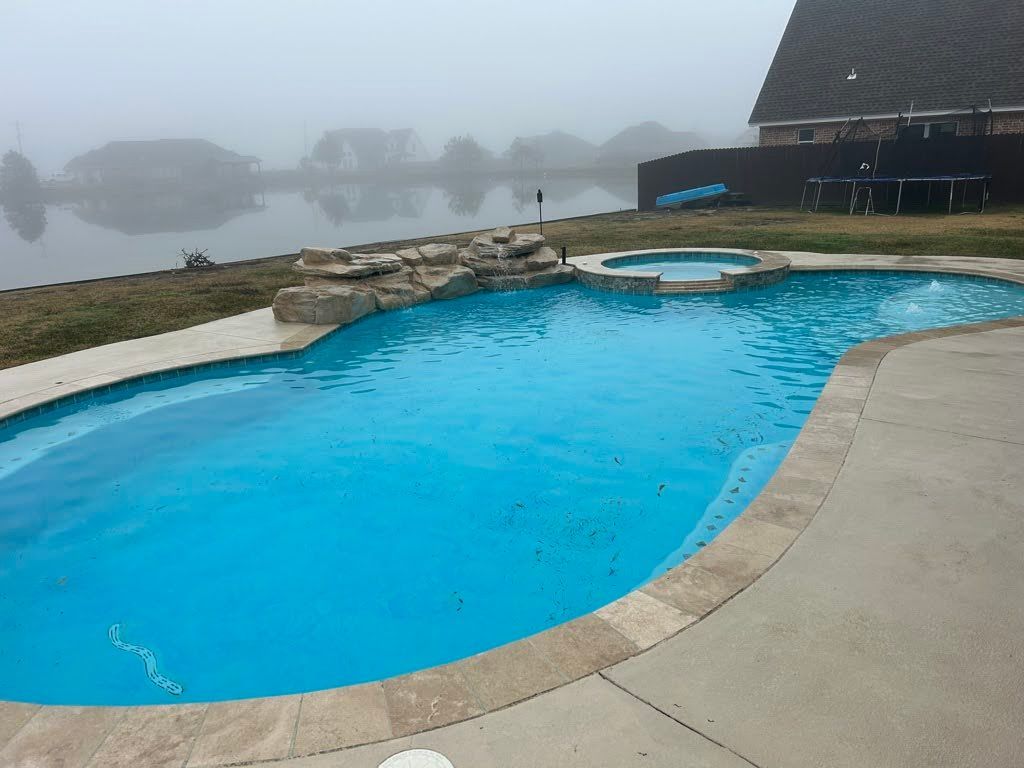 A large swimming pool with a hot tub next to a lake on a foggy day.