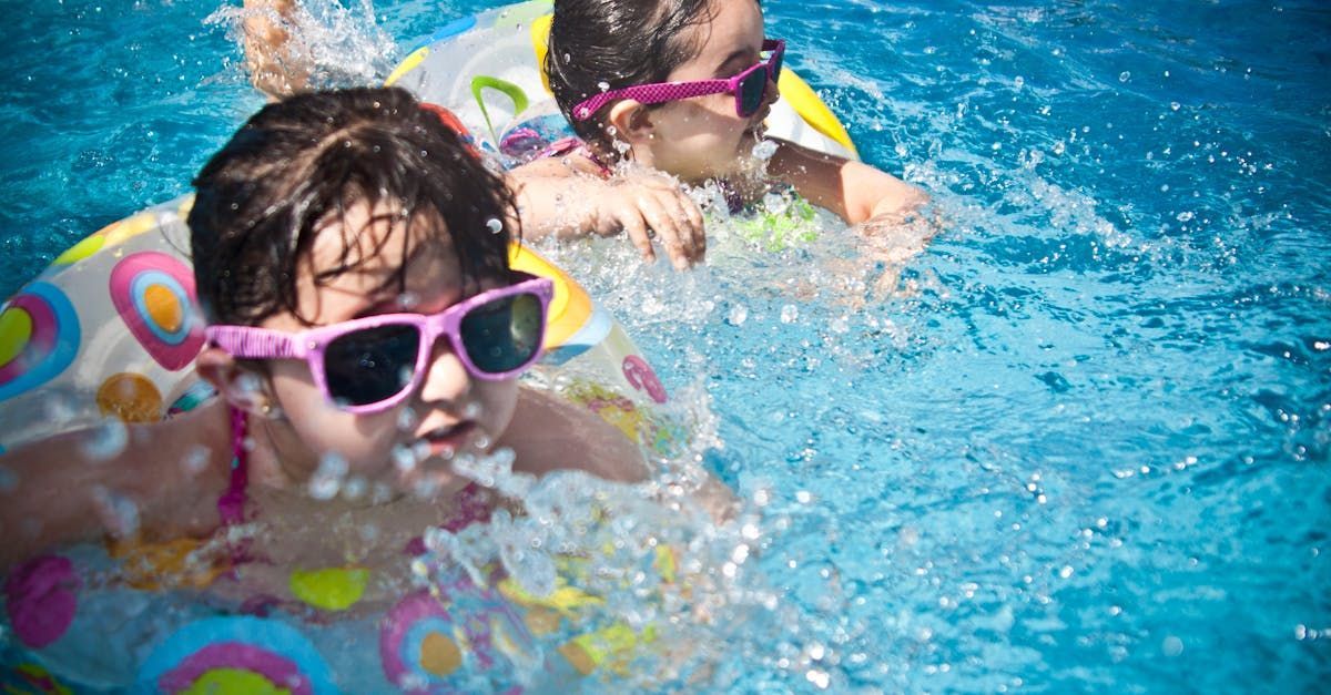 Two young girls wearing sunglasses are floating in a swimming pool.