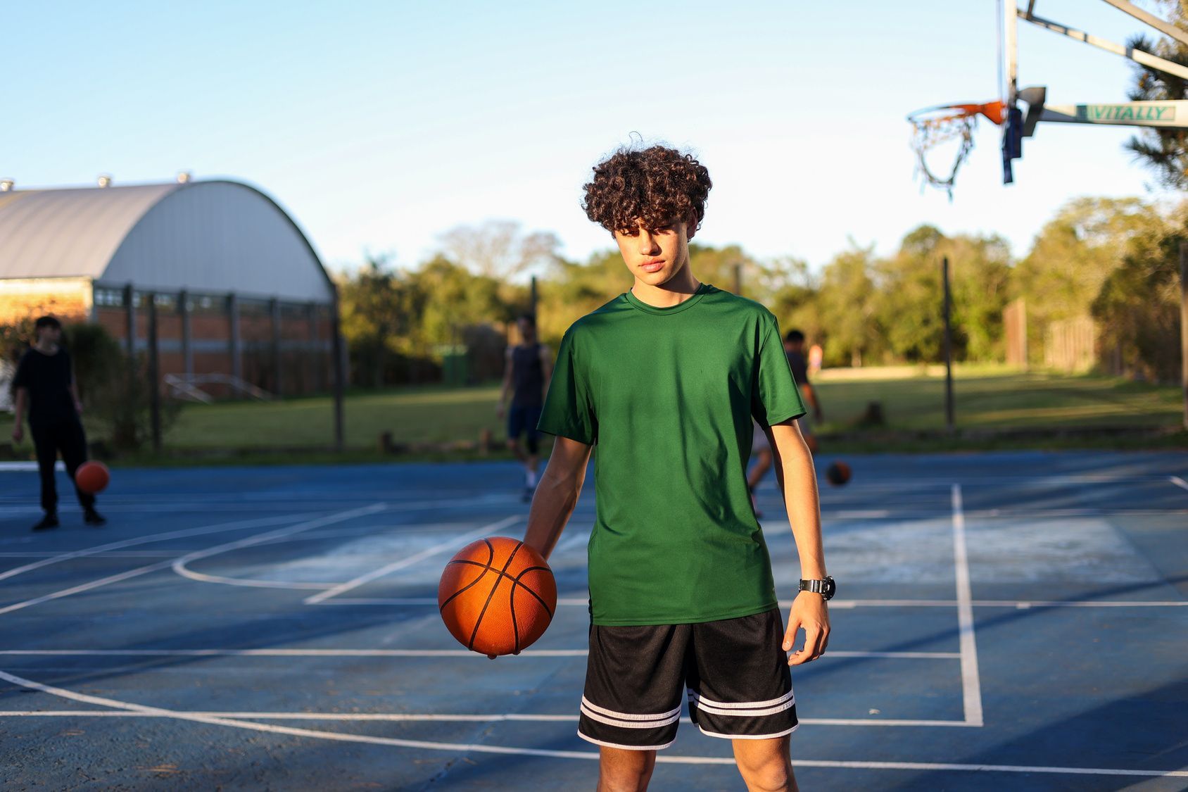 A person wearing a hat and orange shirt, holding a baseball bat on their shoulder on a baseball field.