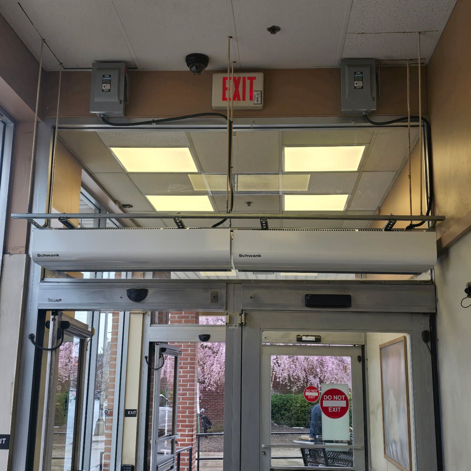 Entrance door with overhead exit sign, security cameras, speakers, and air curtains.