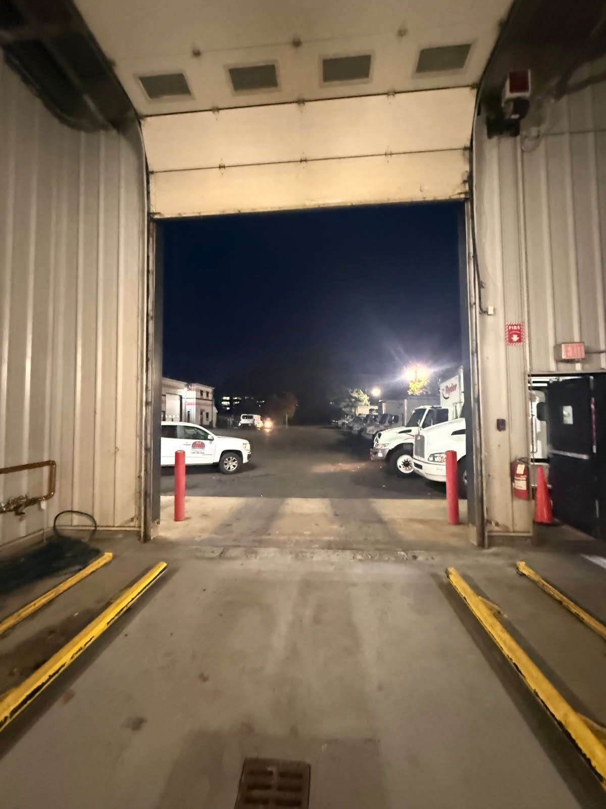 View from inside a garage looking out at white trucks parked along a driveway at night.