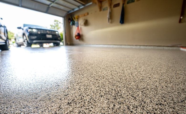 Garage with a speckled floor and an open door showing a parked vehicle outside