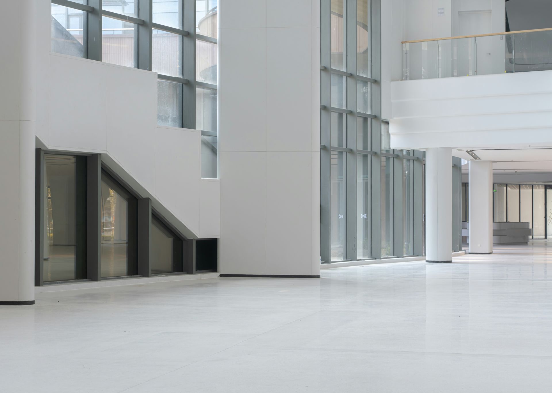 Modern atrium interior with white floors, tall glass walls, and a staircase