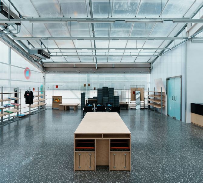 Spacious studio with a long wooden table, shelves, black seating, and a glass garage door.