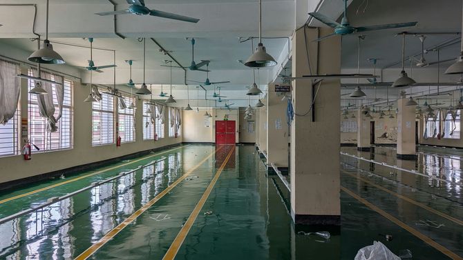 Abandoned indoor pool with green water, peeling paint, and rows of windows and ceiling fans