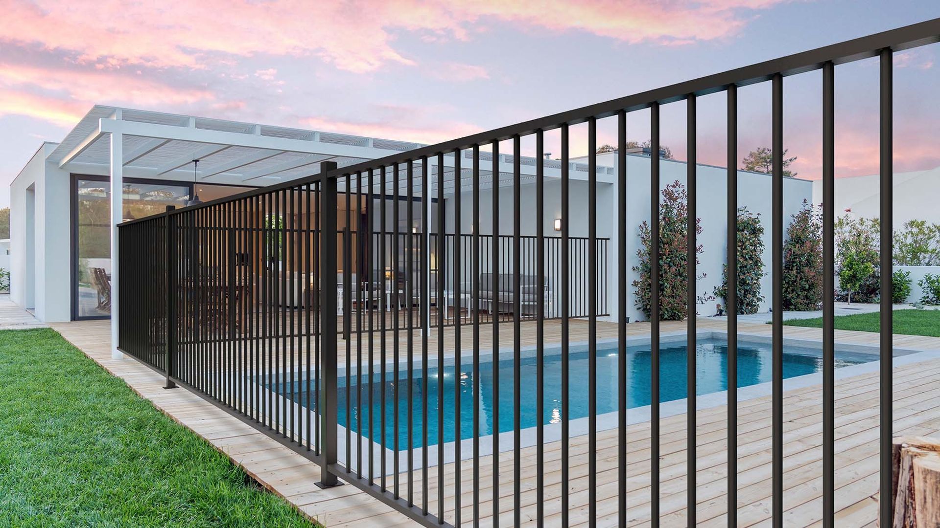 Modern backyard with a fenced swimming pool beside a covered patio at sunset