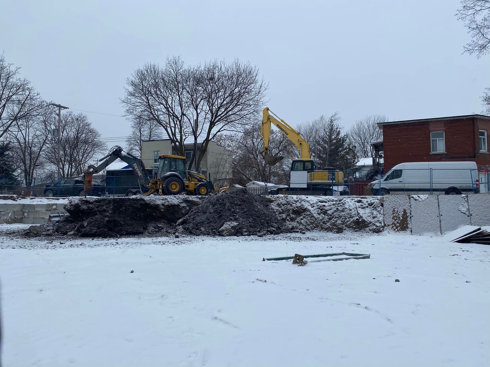 Un chantier dans la neige avec une excavatrice jaune et une camionnette blanche.