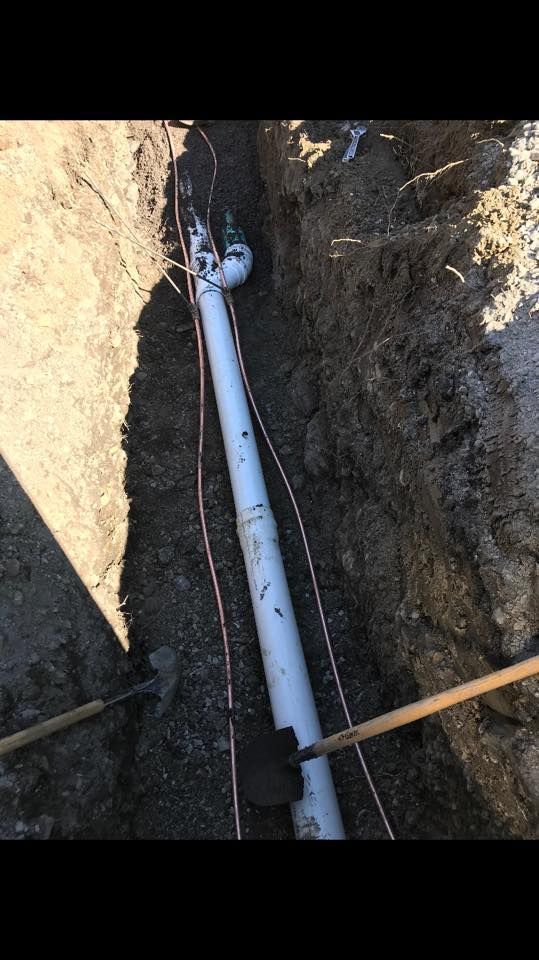 Un tuyau blanc est posé dans la terre à côté d'une pelle.