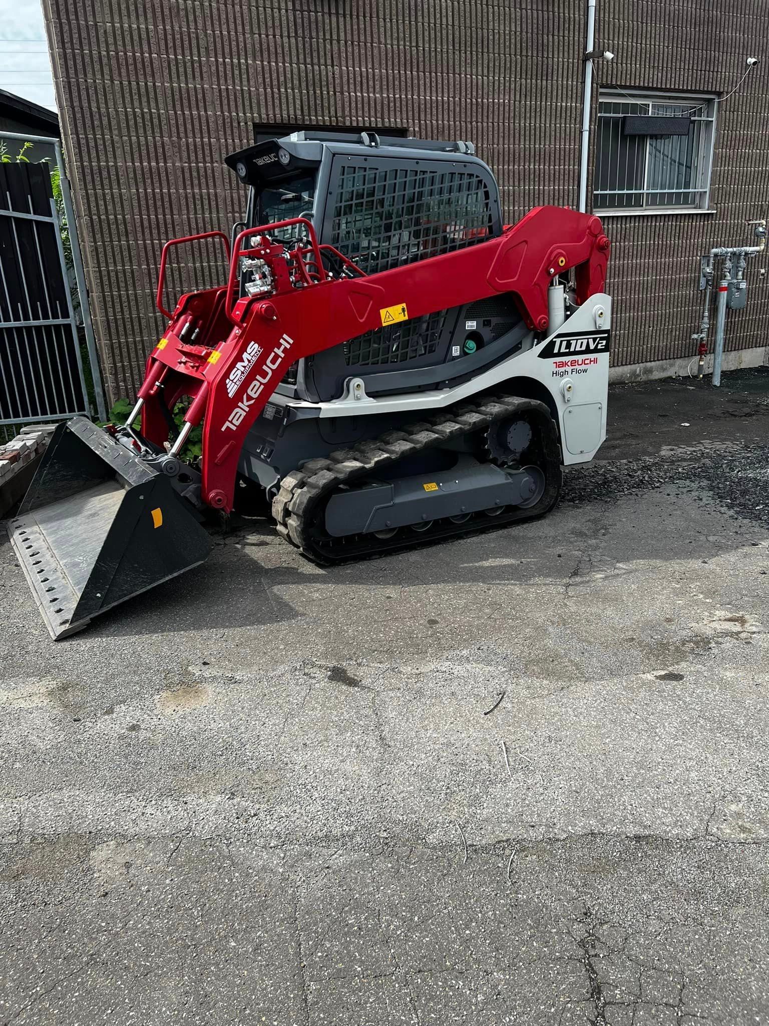 Un bulldozer rouge et blanc est garé devant un bâtiment.