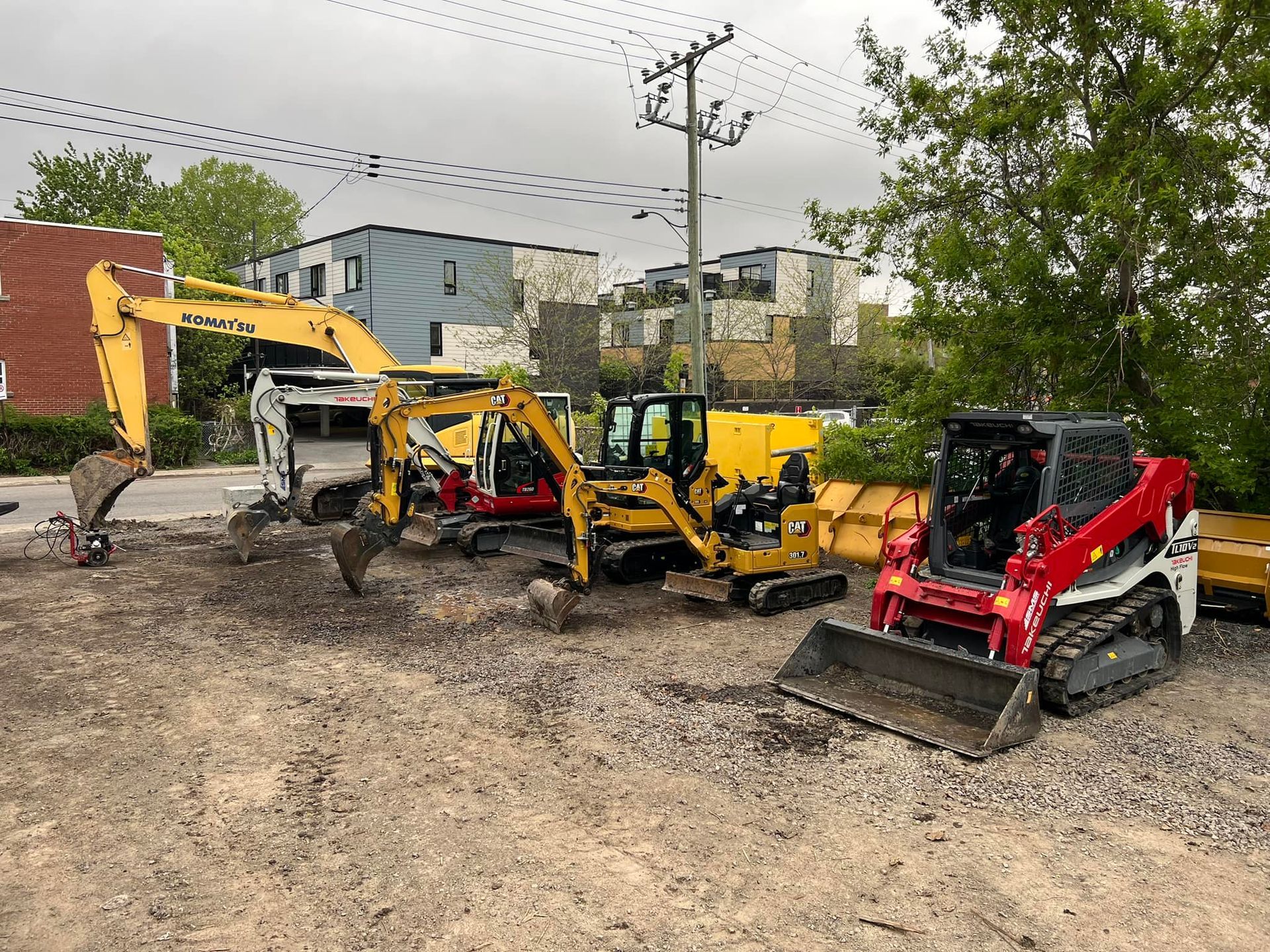 Une rangée de véhicules de construction est garée sur un terrain en terre.