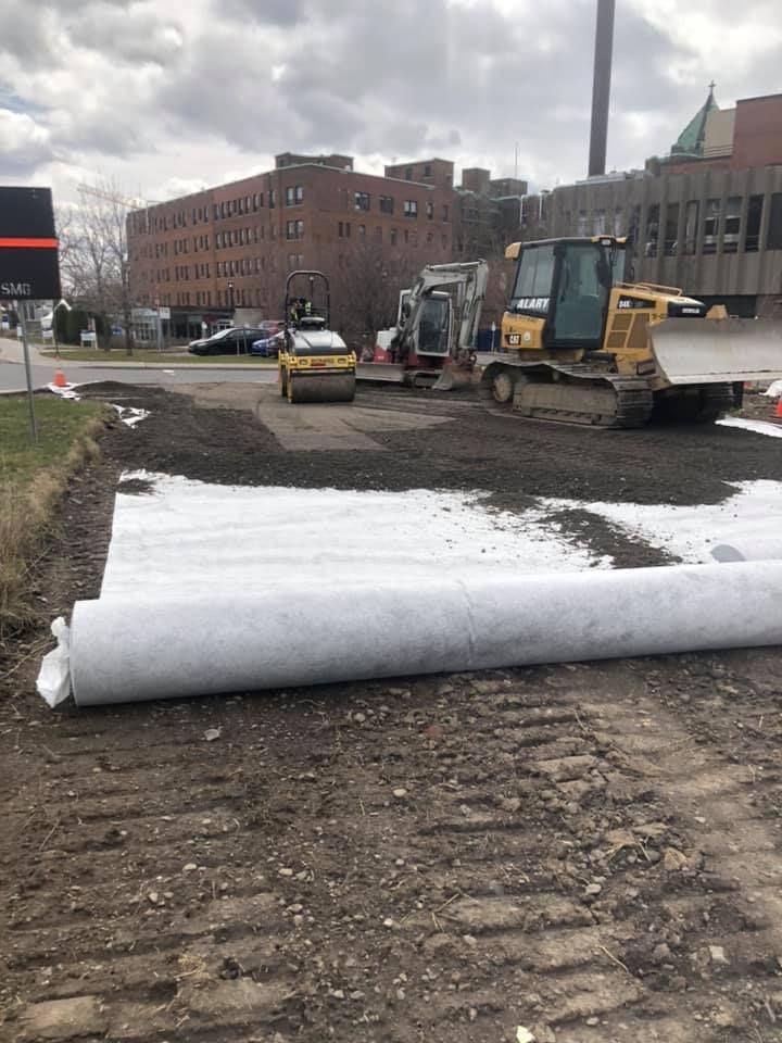 Un bulldozer pose un rouleau de géotextile sur le sol.