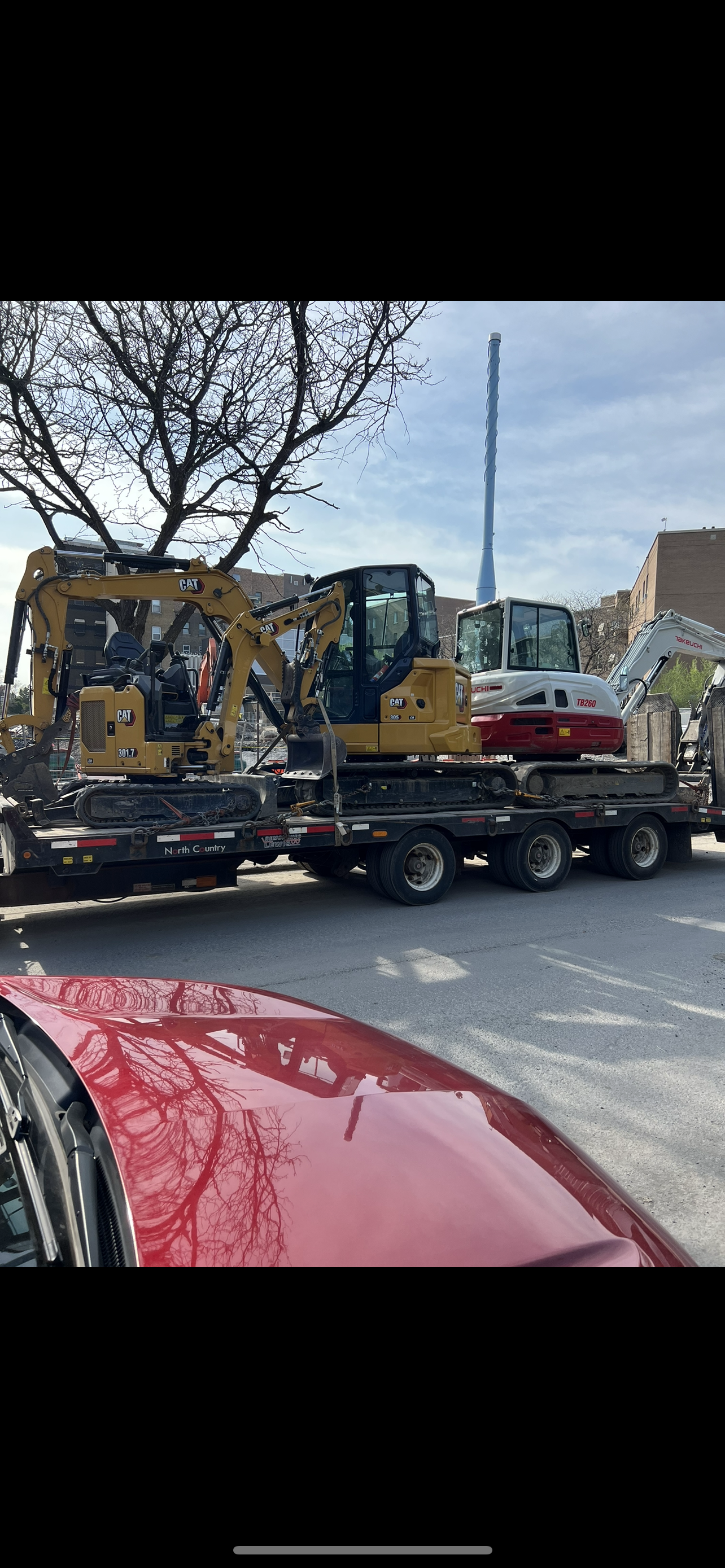 Une voiture rouge est garée à côté d'un camion avec un bulldozer dessus.