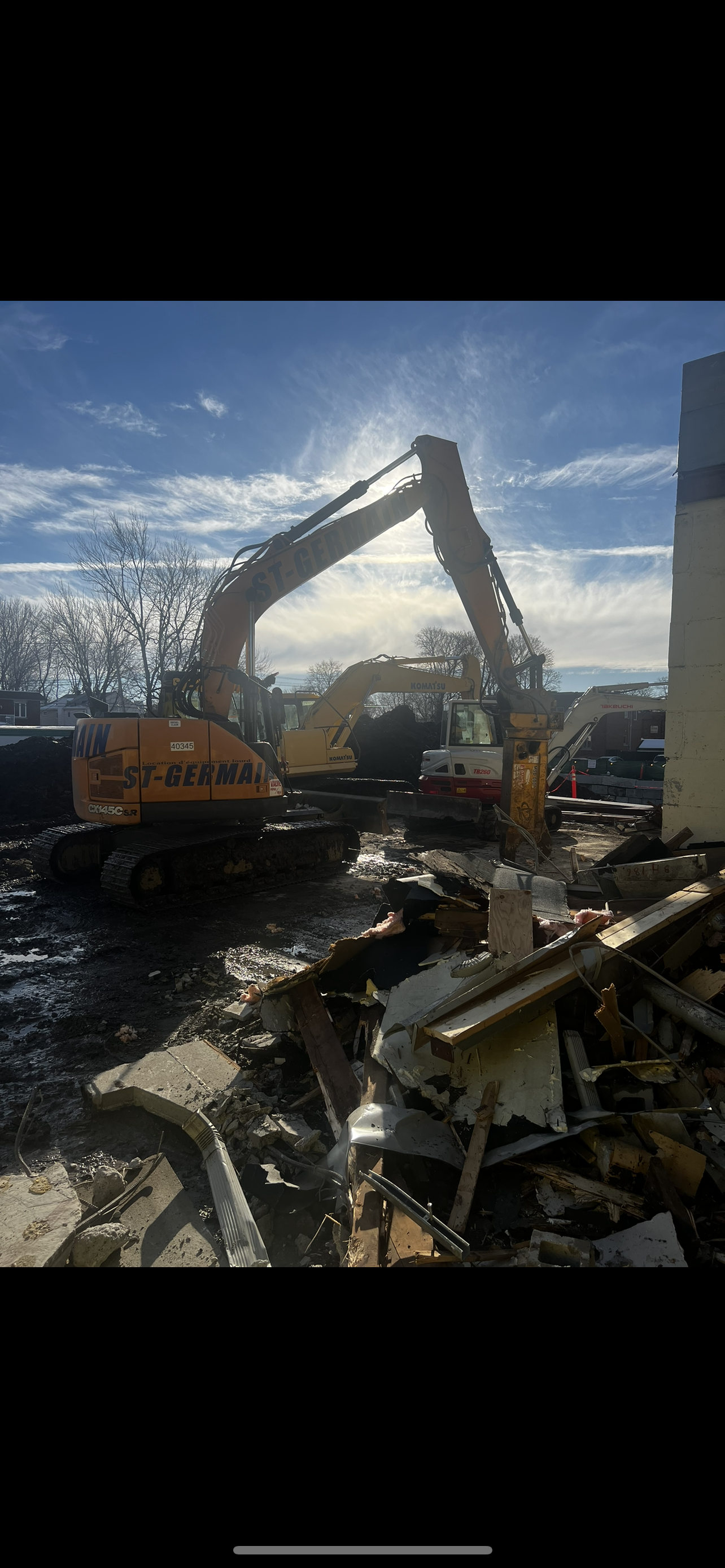 Une grande excavatrice jaune démolit un bâtiment.