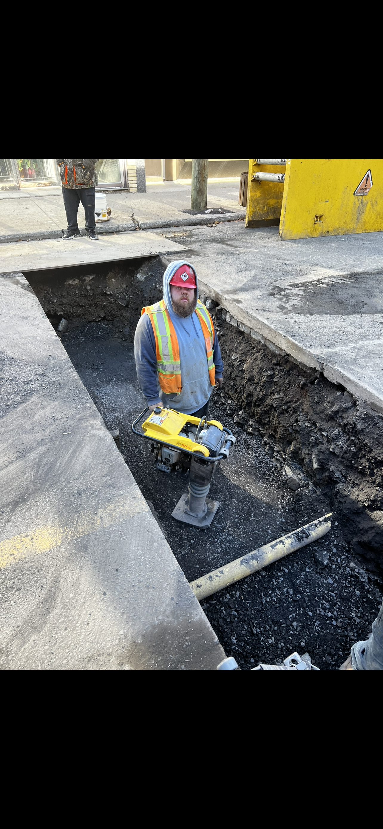 Un ouvrier du bâtiment est assis dans un trou dans le sol et tient une pelle.