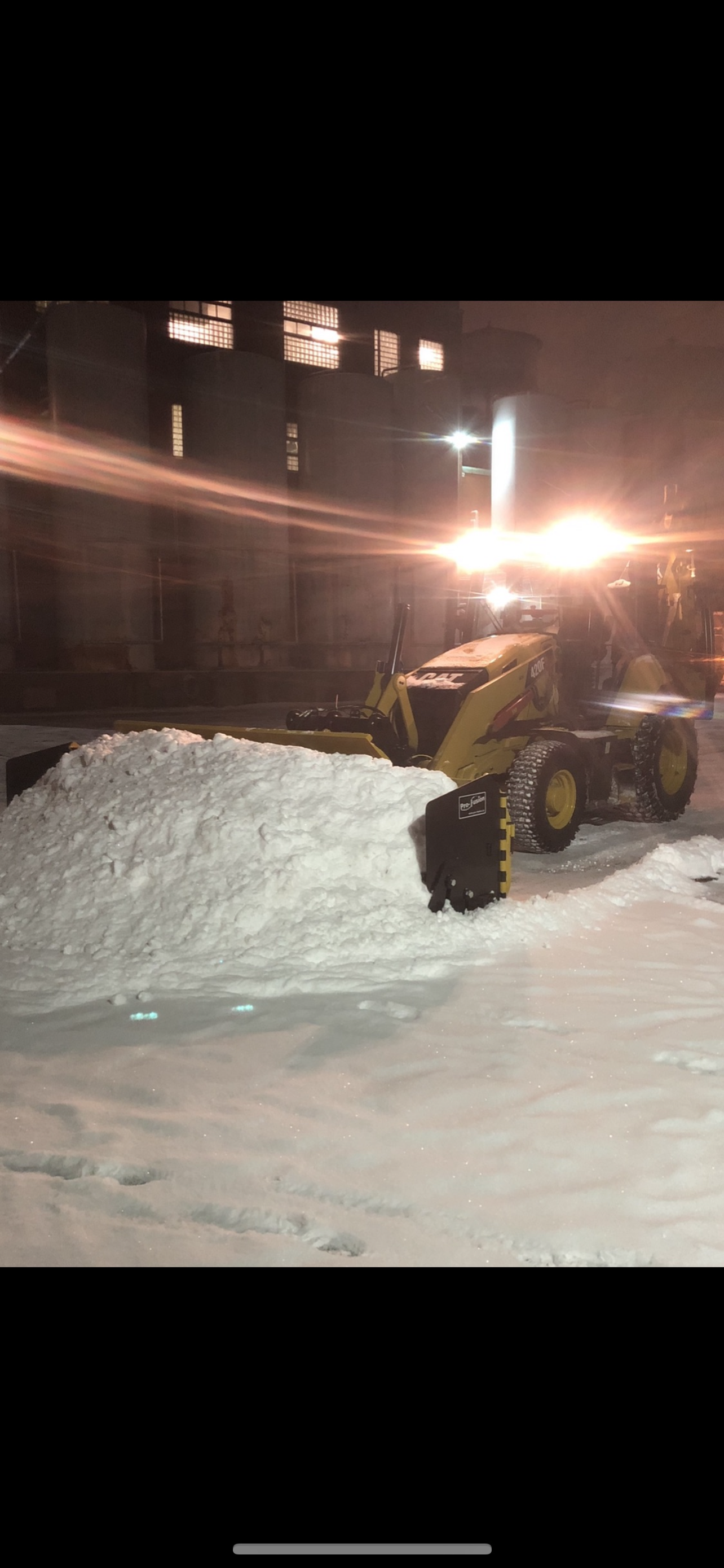 Un chasse-neige déblaye la neige d'un parking la nuit.