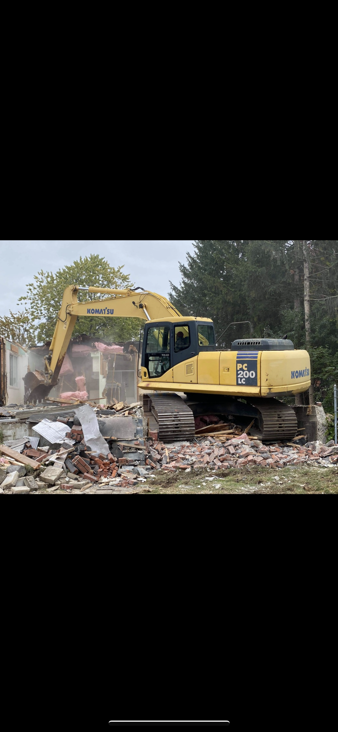 Une excavatrice jaune démolit un bâtiment.