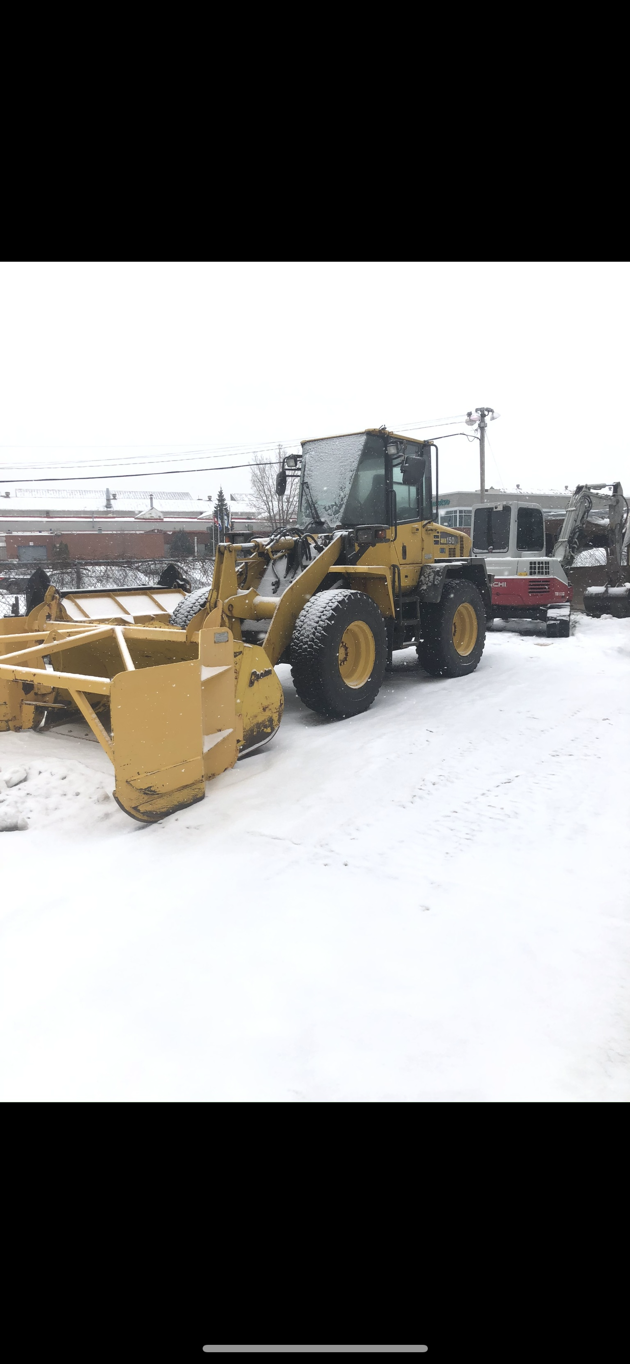 Un tracteur jaune est garé dans la neige sur un parking.