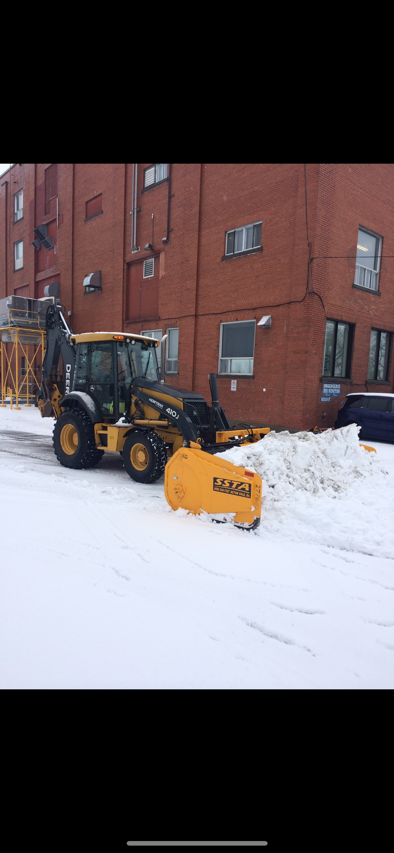 Un chasse-neige jaune déneige devant un bâtiment en briques.