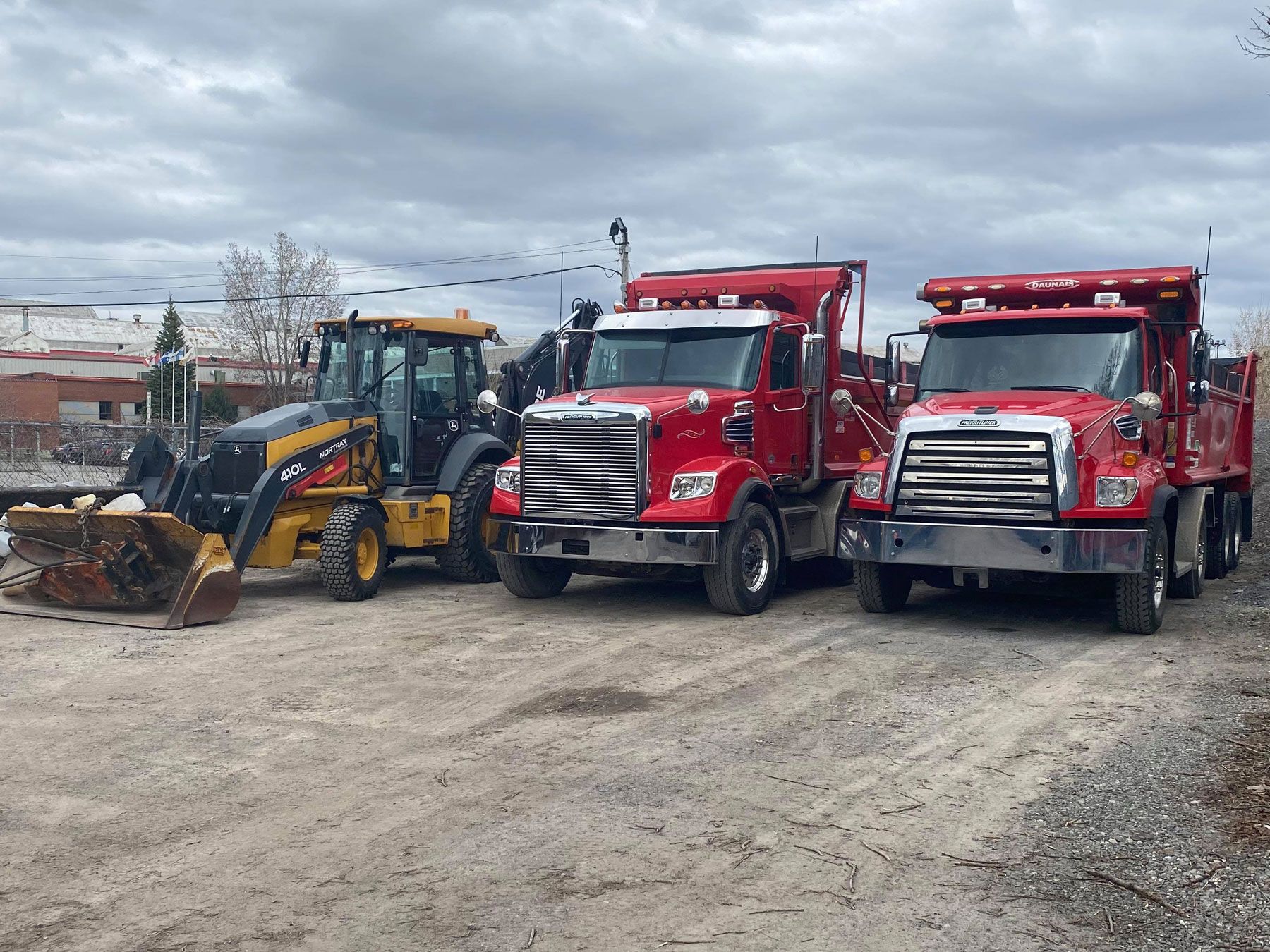 Trois camions à benne basculante rouges sont garés l'un à côté de l'autre sur un chemin de terre.