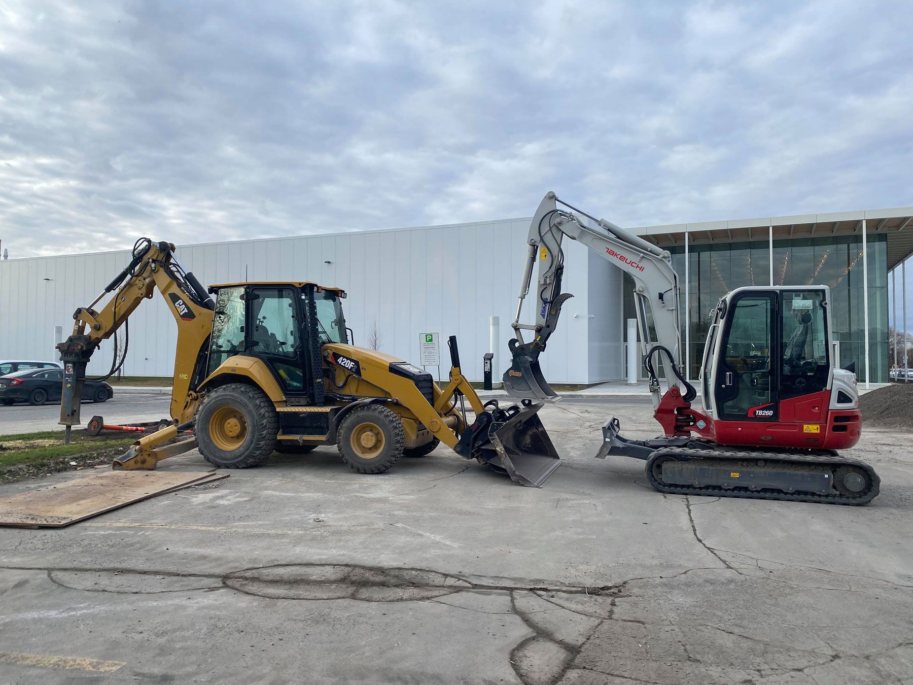 Deux véhicules de chantier sont garés sur un parking devant un bâtiment.