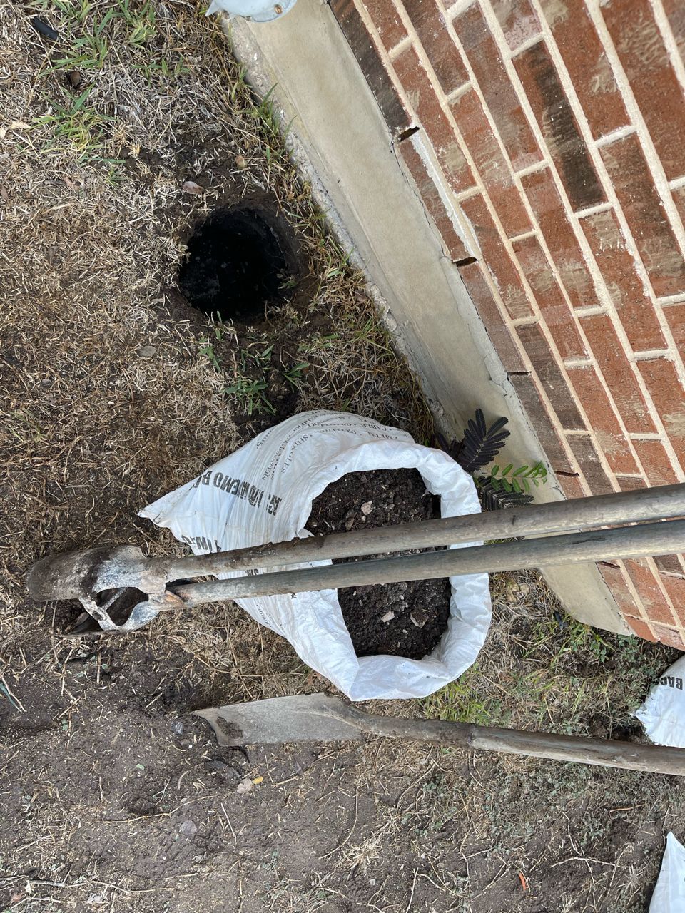 A shovel and a bag of dirt are sitting next to a brick wall.