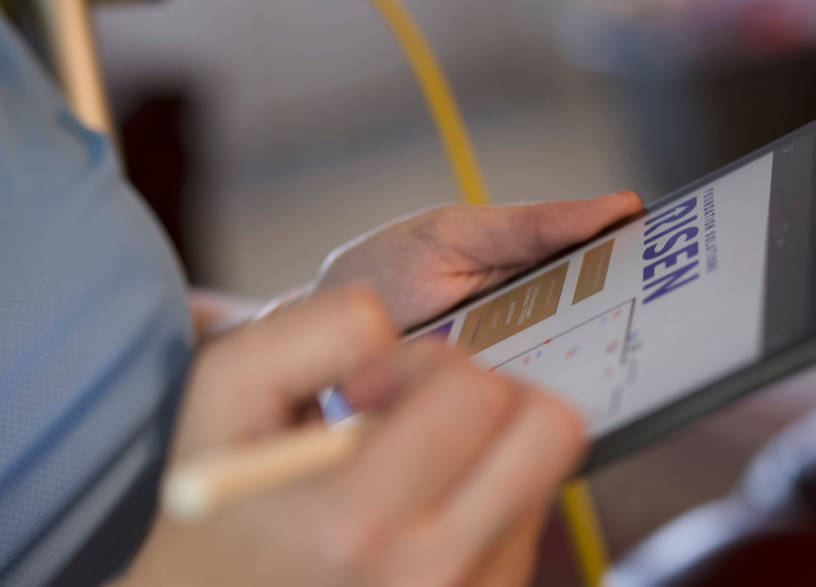 A hand uses a stylus to work on a tablet screen displaying a floor plan and the word
