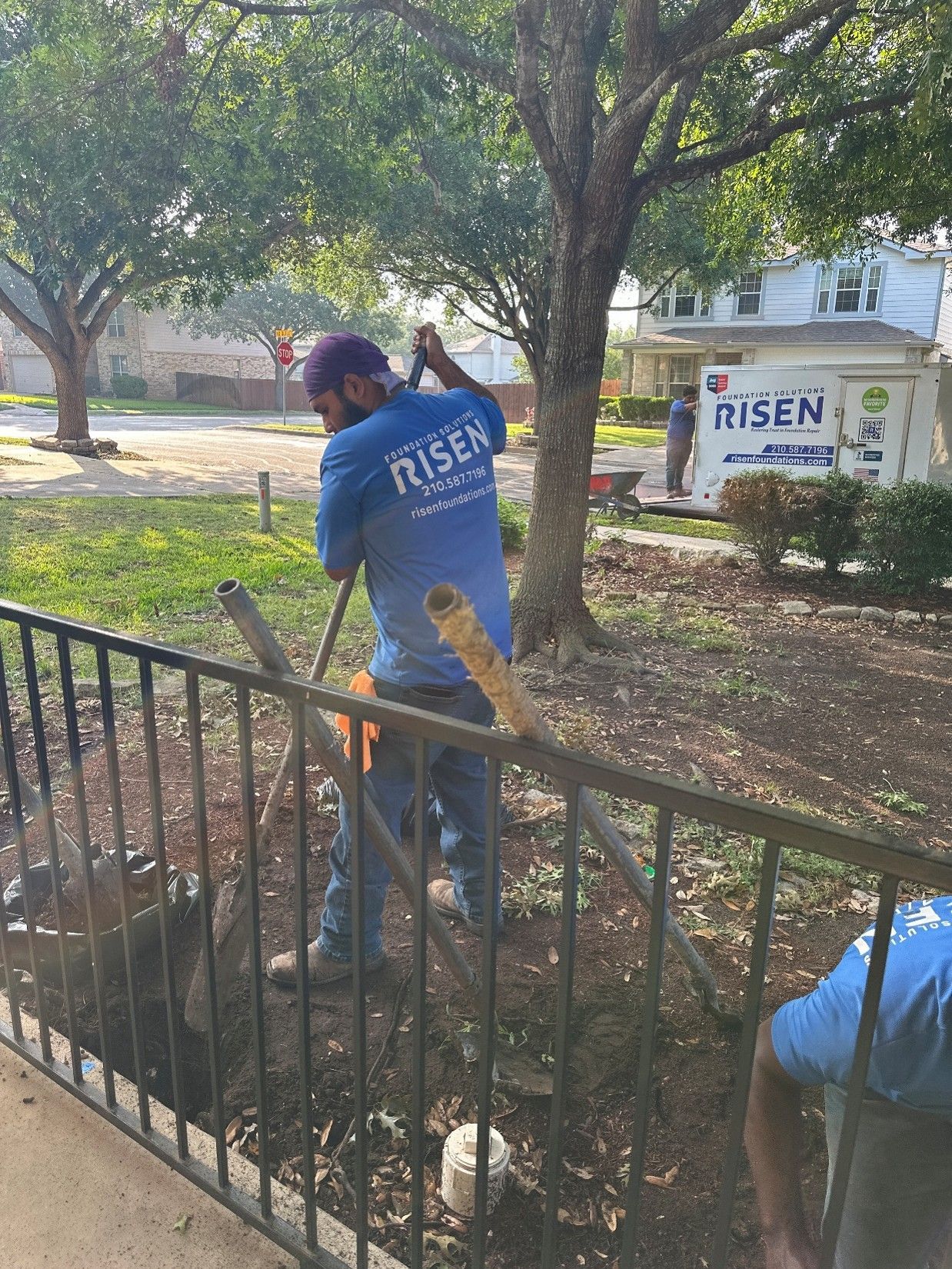 A worker from Risen Foundation Solutions is digging in a yard near a fence