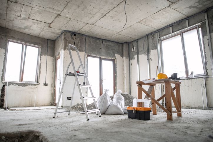 Interior construction site with ladder, windows, work table, and tools. Unfinished walls and concrete floor. Interior construction site with ladder, windows, work table, and tools. Unfinished walls and concrete floor.