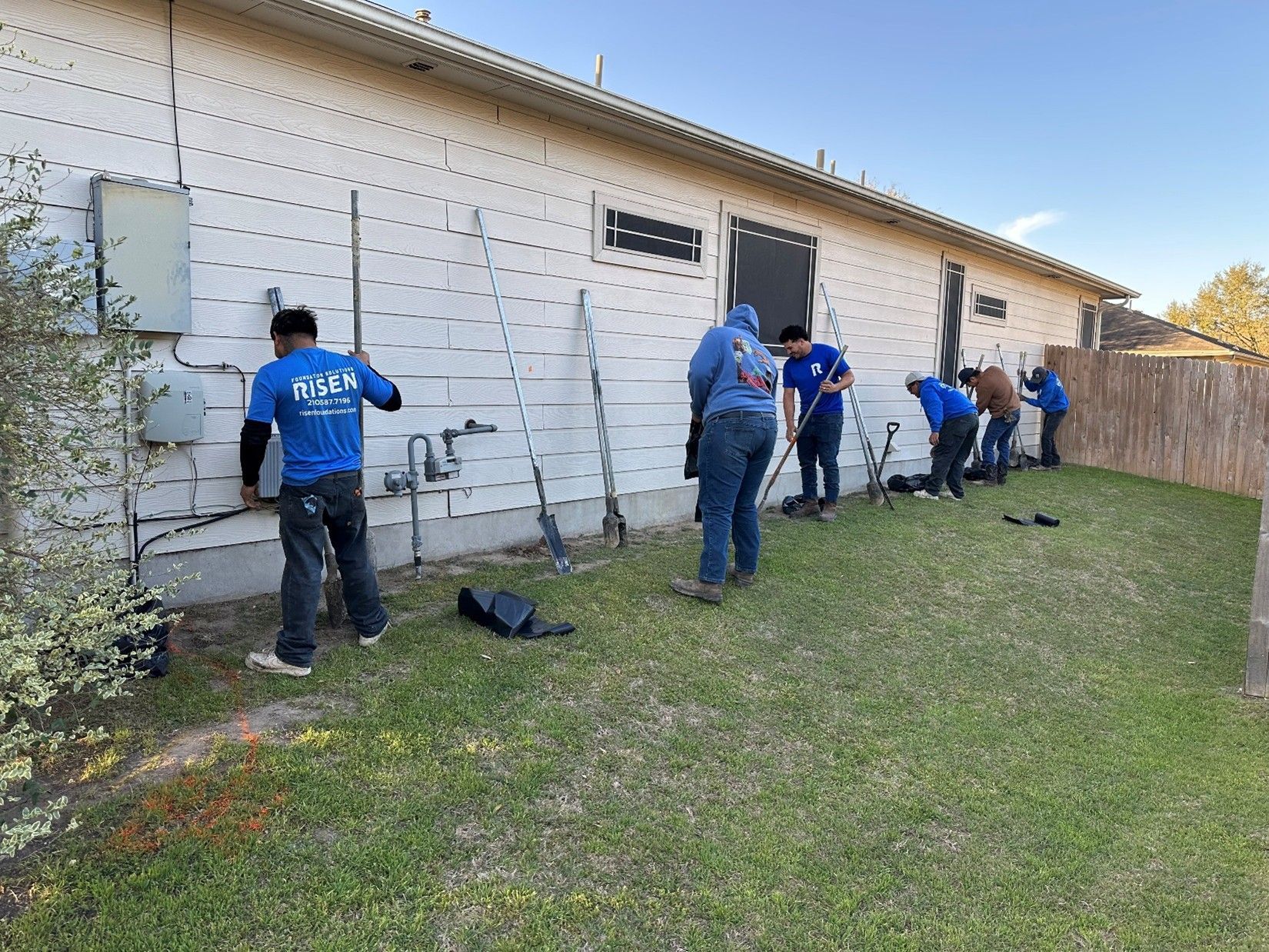 A group of people working on a house's exterior. They are on the lawn near a fence. A group of people working on a house's exterior. They are on the lawn near a fence.