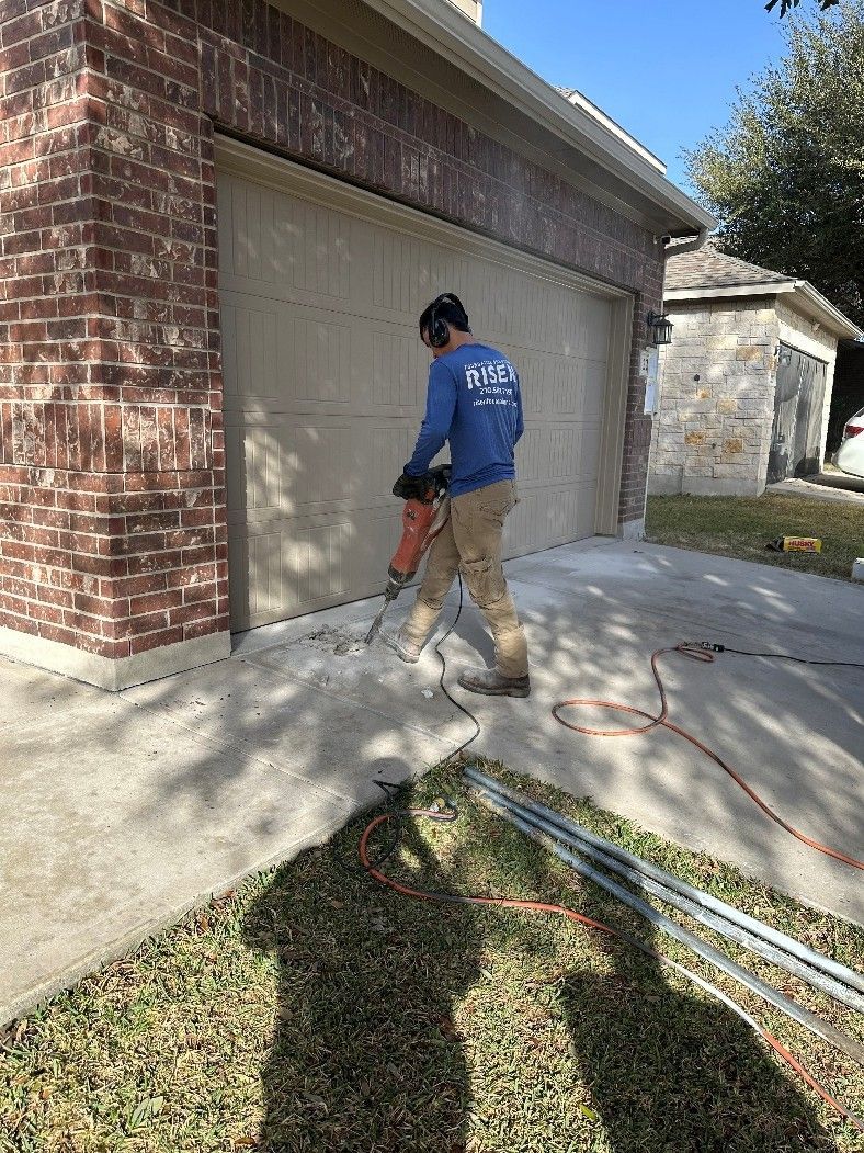 Construction worker using a jackhammer on concrete near a brick building with a garage door Construction worker using a jackhammer on concrete near a brick building with a garage door