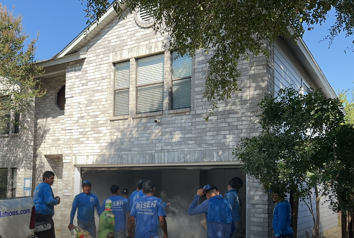 A group of people are standing in front of a white brick house.