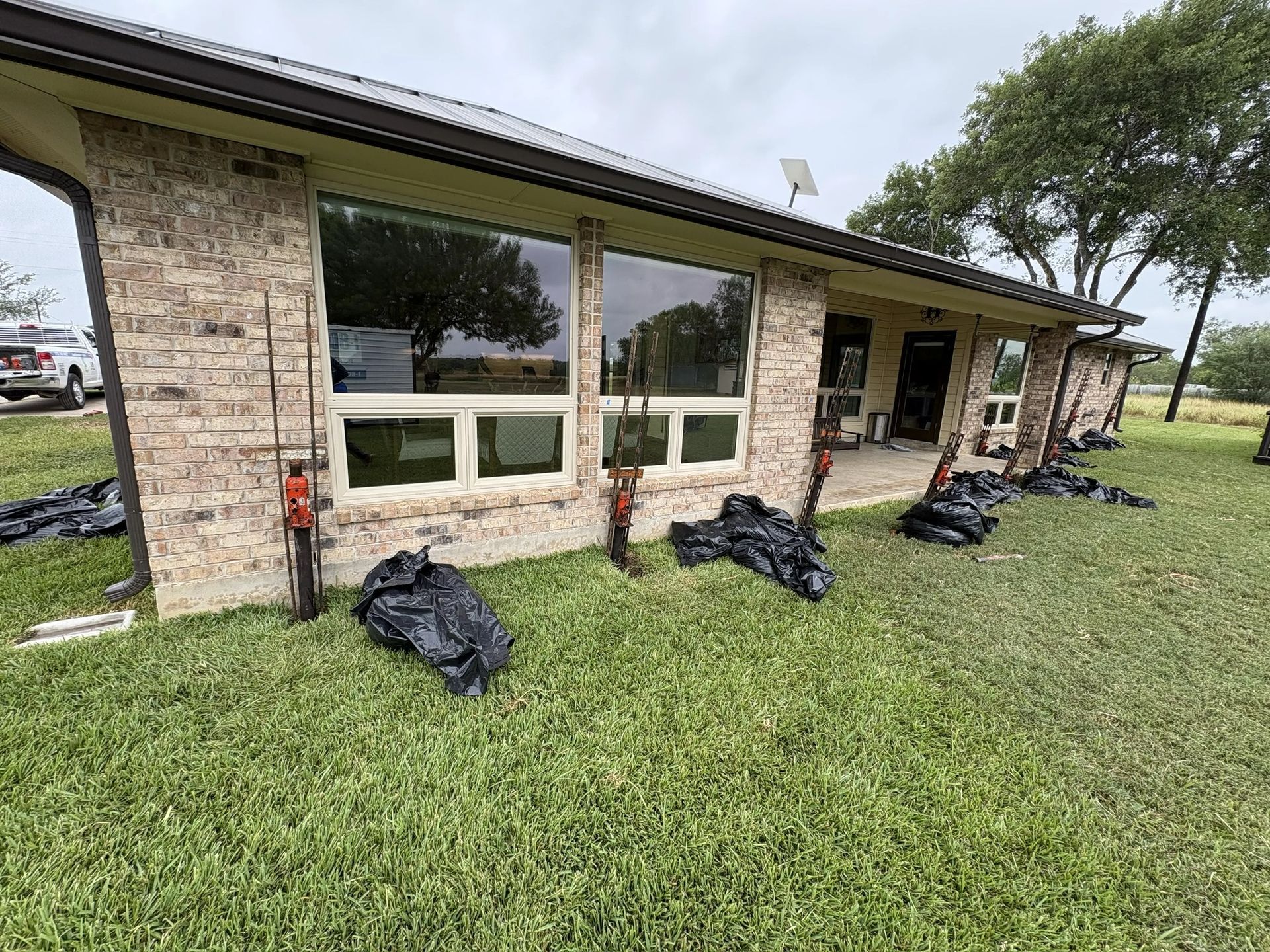 Brick house with storm-damaged roof and windows, bags of debris on the lawn, and a tree in the yard