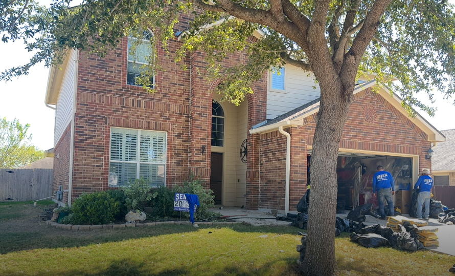 Brick house exterior with three workers removing debris from garage, sunny day.