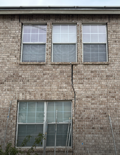 Brick house exterior with a large vertical crack running down the wall between windows. Brick house exterior with a large vertical crack running down the wall between windows.