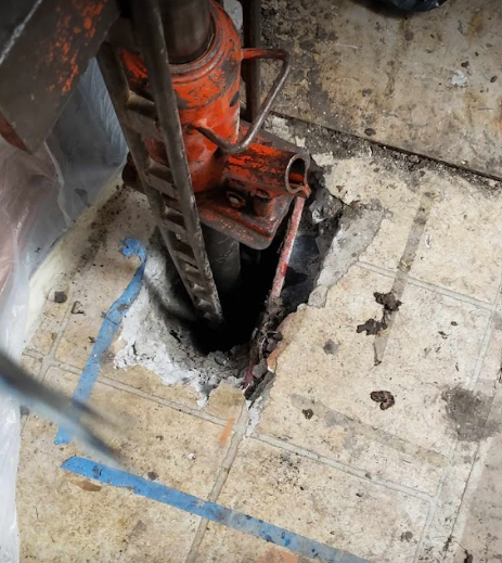 A hydraulic jack is sitting in a hole in the floor.