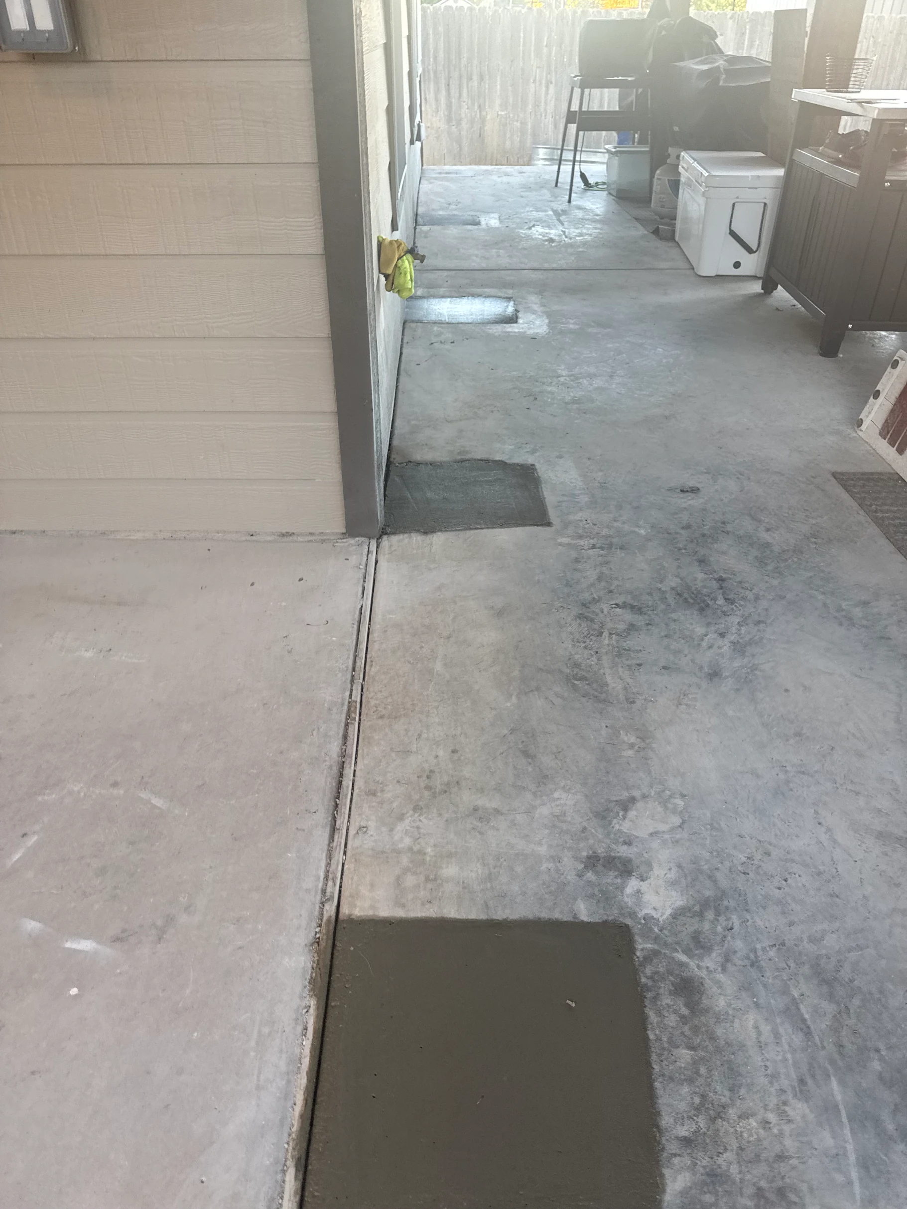 Concrete patio with recent repairs; a building's exterior on the left, outdoor setting.