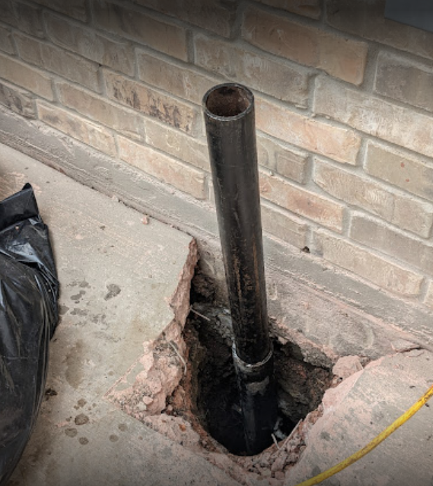A pipe is sticking out of a hole in a brick wall.