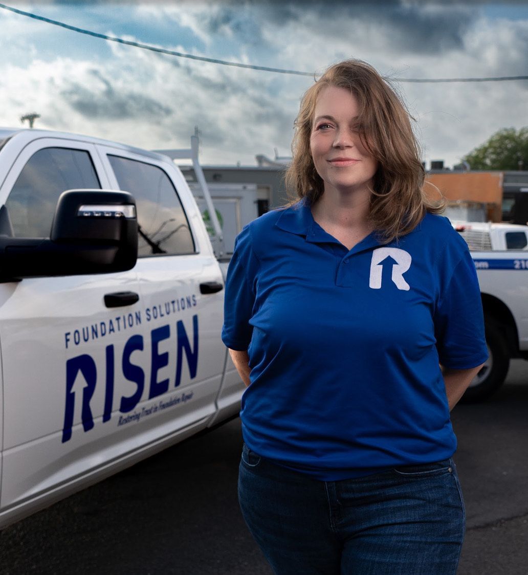 A woman in a blue shirt is standing in front of a white truck that says risen
